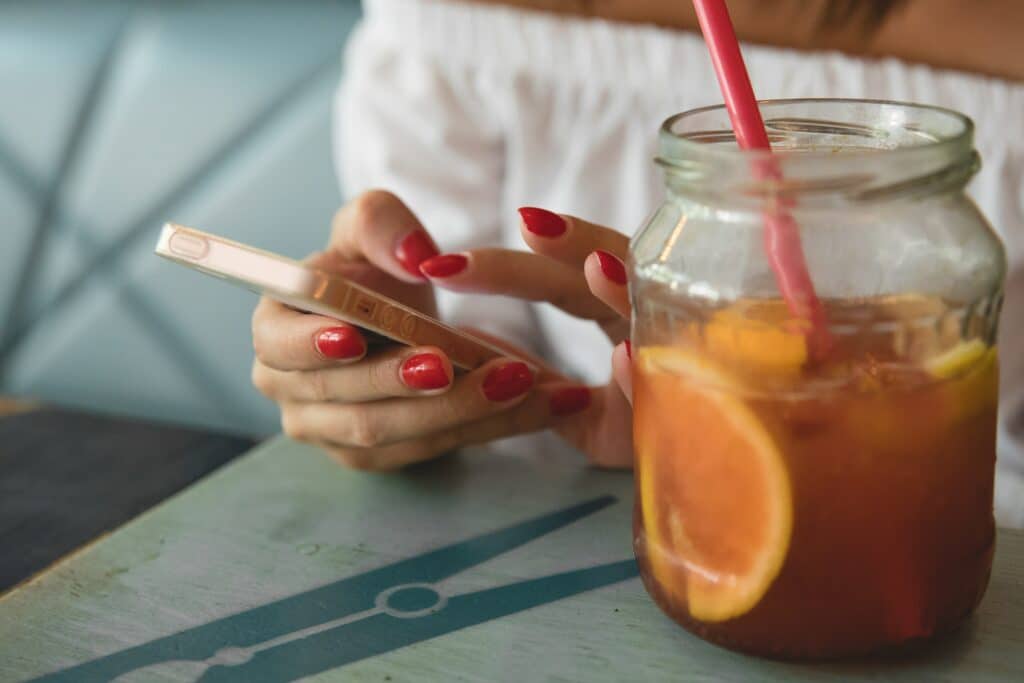 woman typing on phone next to masonry jar filled with iced tea