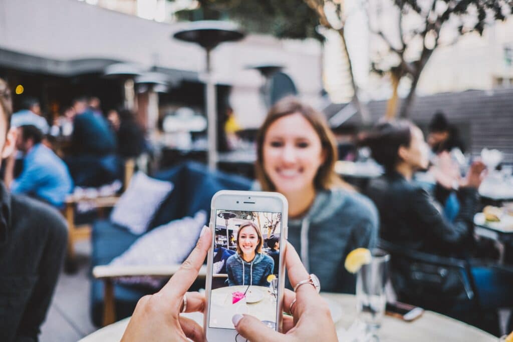 first person view taking a photo with your phone of a young woman sitting at the table across from you sitting in a cafe